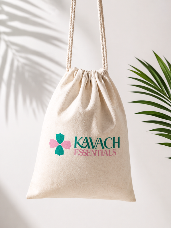 A beige cotton drawstring bag with rope handles, featuring the 'KAVACH ESSENTIALS' logo in green and pink. The bag is hanging against a white wall with palm leaf shadows on the left and a green plant leaf on the right.