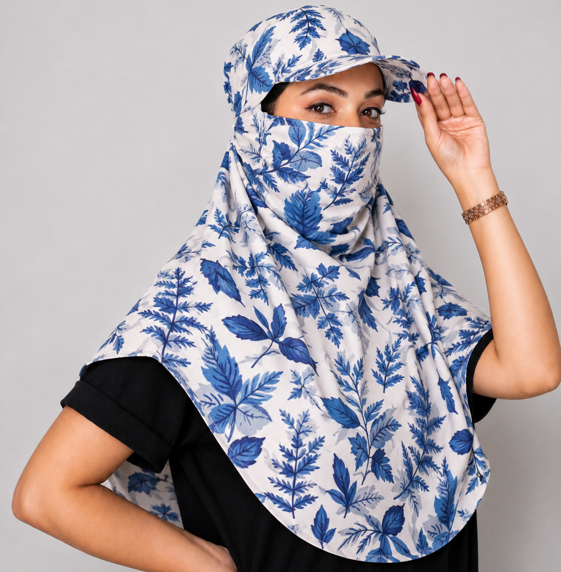 A woman wearing a white and blue leaf-patterned face scarf and matching face cover, posed against a solid gray studio background.