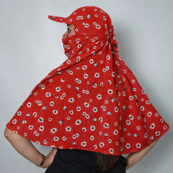 A women shown from the back wearing a red color sun protection scarf with a matching face veil and cap, featuring a white and blue daisy floral pattern, against a plain gray background.
