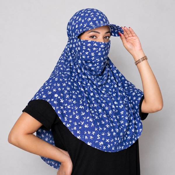A woman wearing a blue and white patterned hijab headscarf with a matching cap, posing against a solid gray studio background.