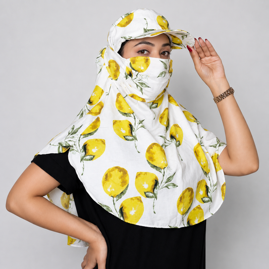 A woman wearing a white sun protection headscarf and matching visor with a yellow lemon print, paired with a black t-shirt, against a solid gray studio background.