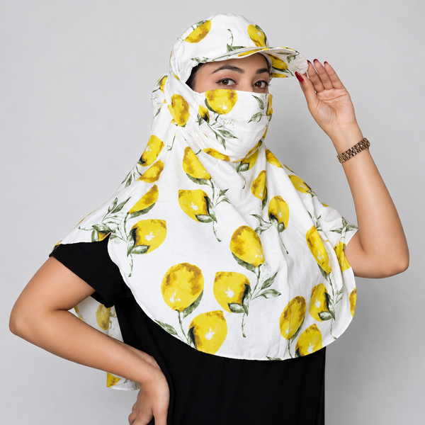 A woman wearing a white sun protection headscarf and matching visor with a yellow lemon print, paired with a black t-shirt, against a solid gray studio background.