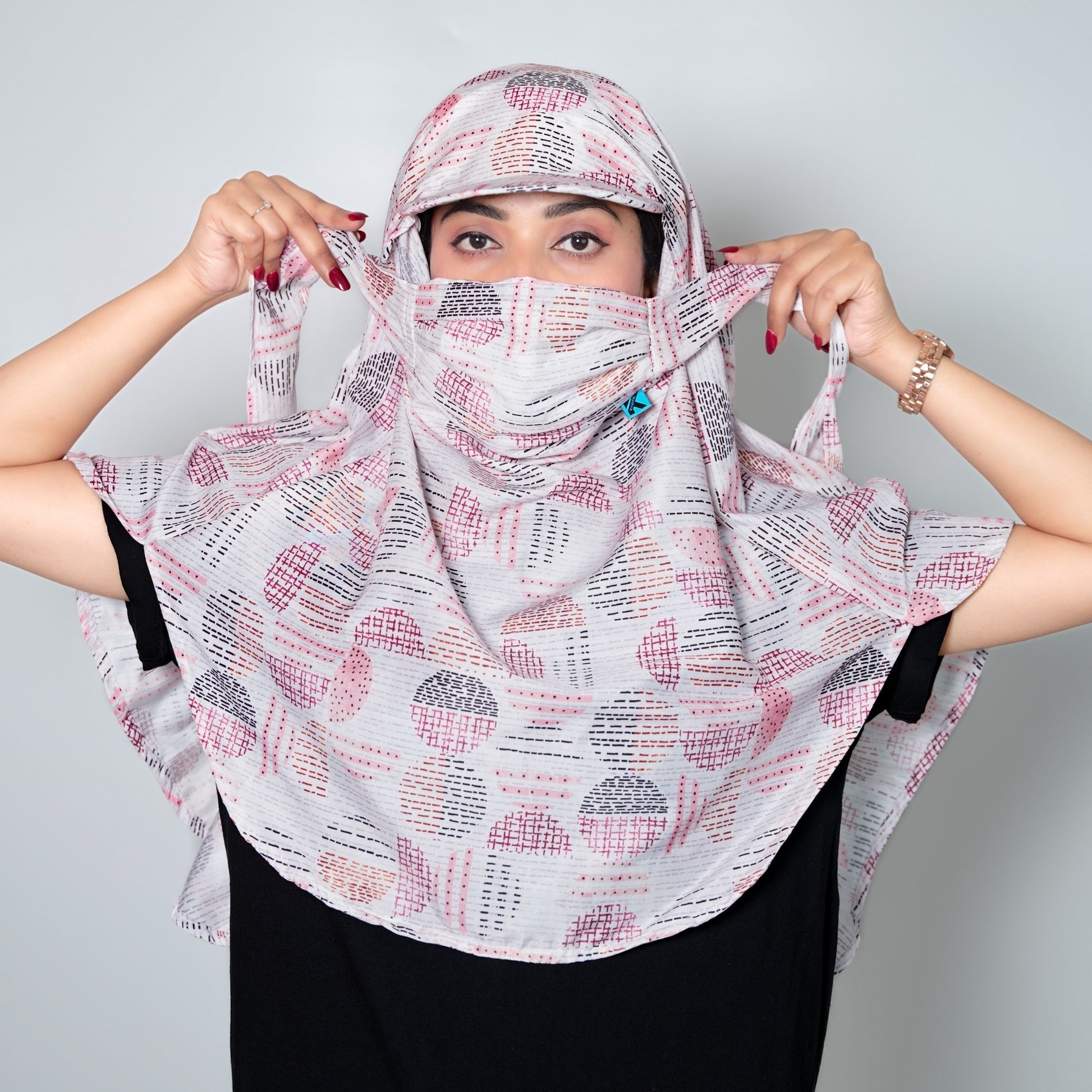 Person wearing a patterned headscarf and face mask against a plain background