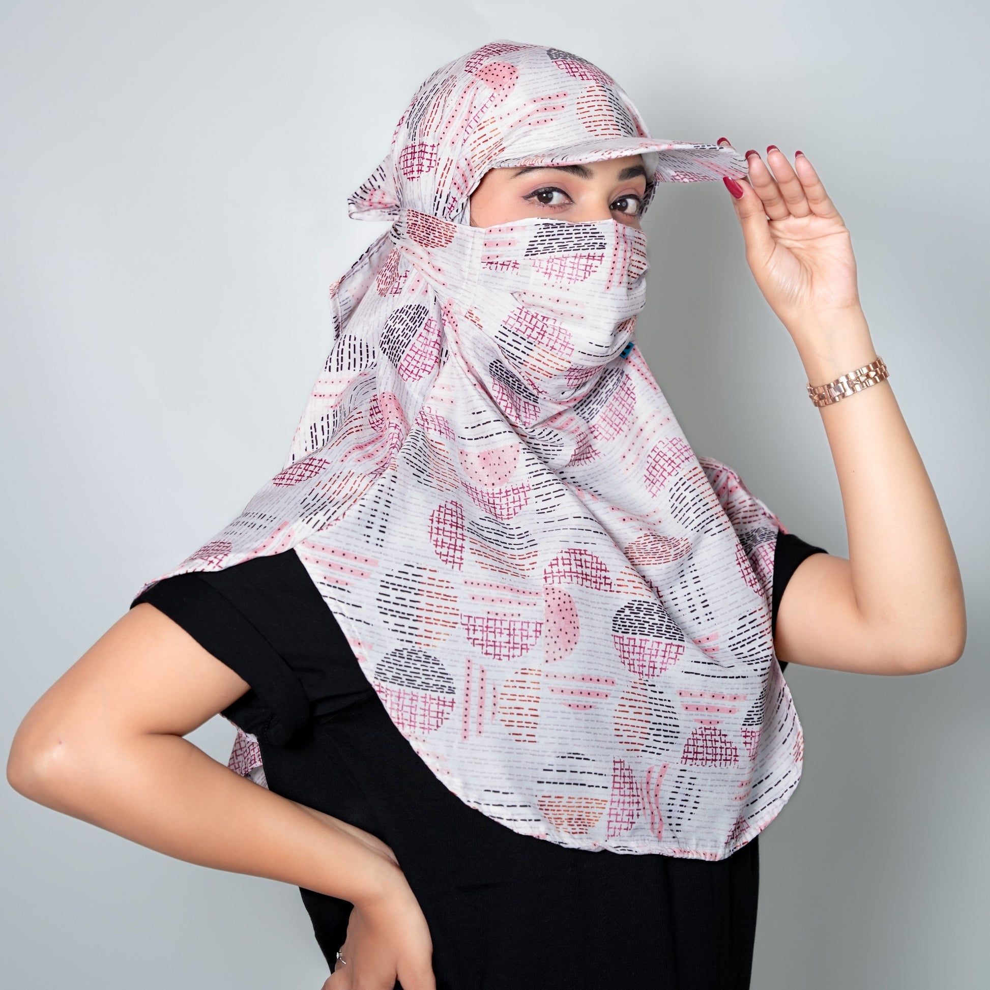 Woman wearing a patterned headscarf and black outfit against a gray background