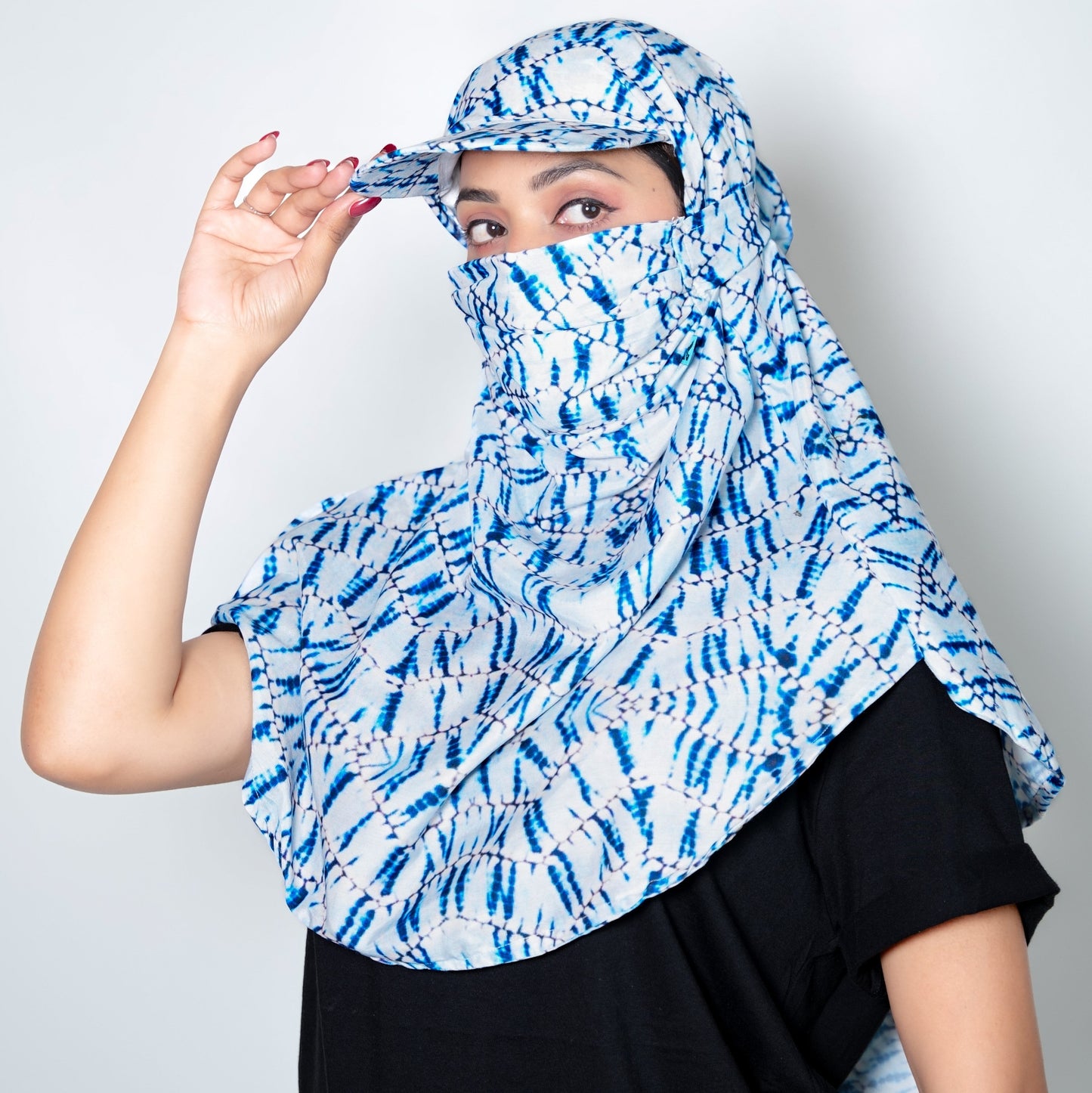 Person wearing a blue and white patterned headscarf and cap against a plain background