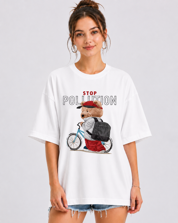 A woman wearing an oversized white graphic t-shirt with a cartoon bear riding a bicycle and the words 'STOP POLLUTION' printed on the front, paired with denim shorts, against a light gray studio background.