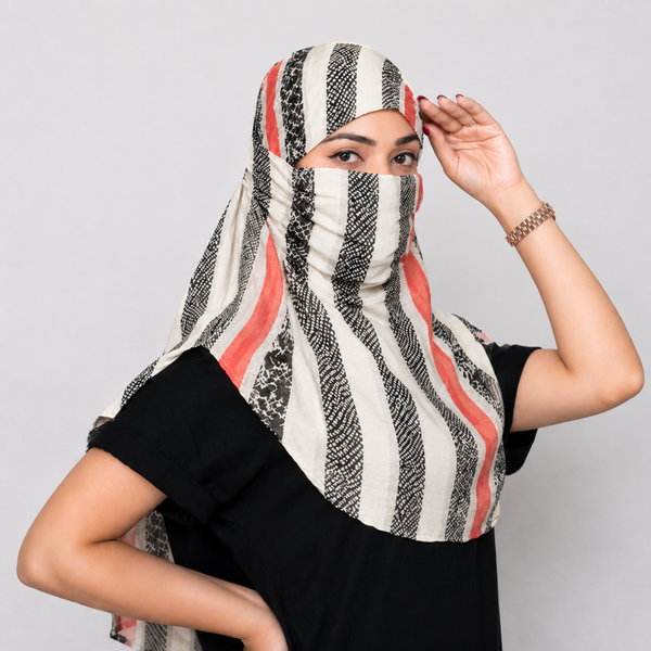 A woman wearing a patterned face scarf with vertical black, white, and coral-red stripes, paired with a black t-shirt against a light gray background.