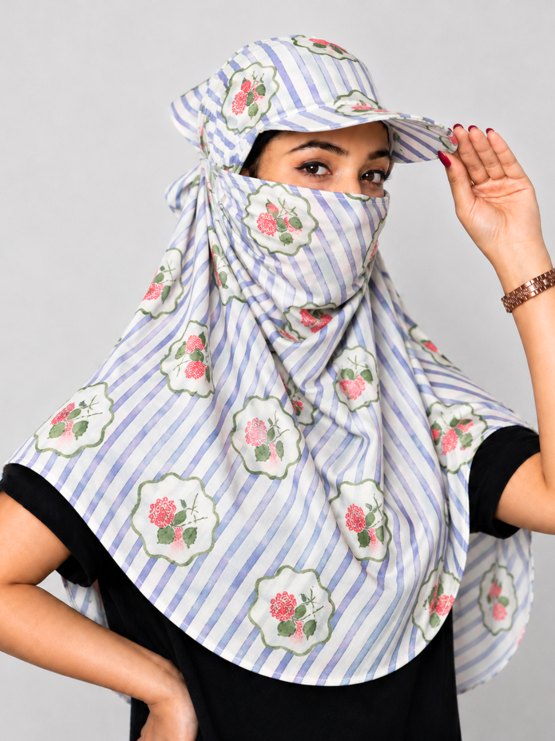 A woman wearing a light blue and white striped face scarf with pink rose motifs and a matching visor, posing against a neutral gray background.