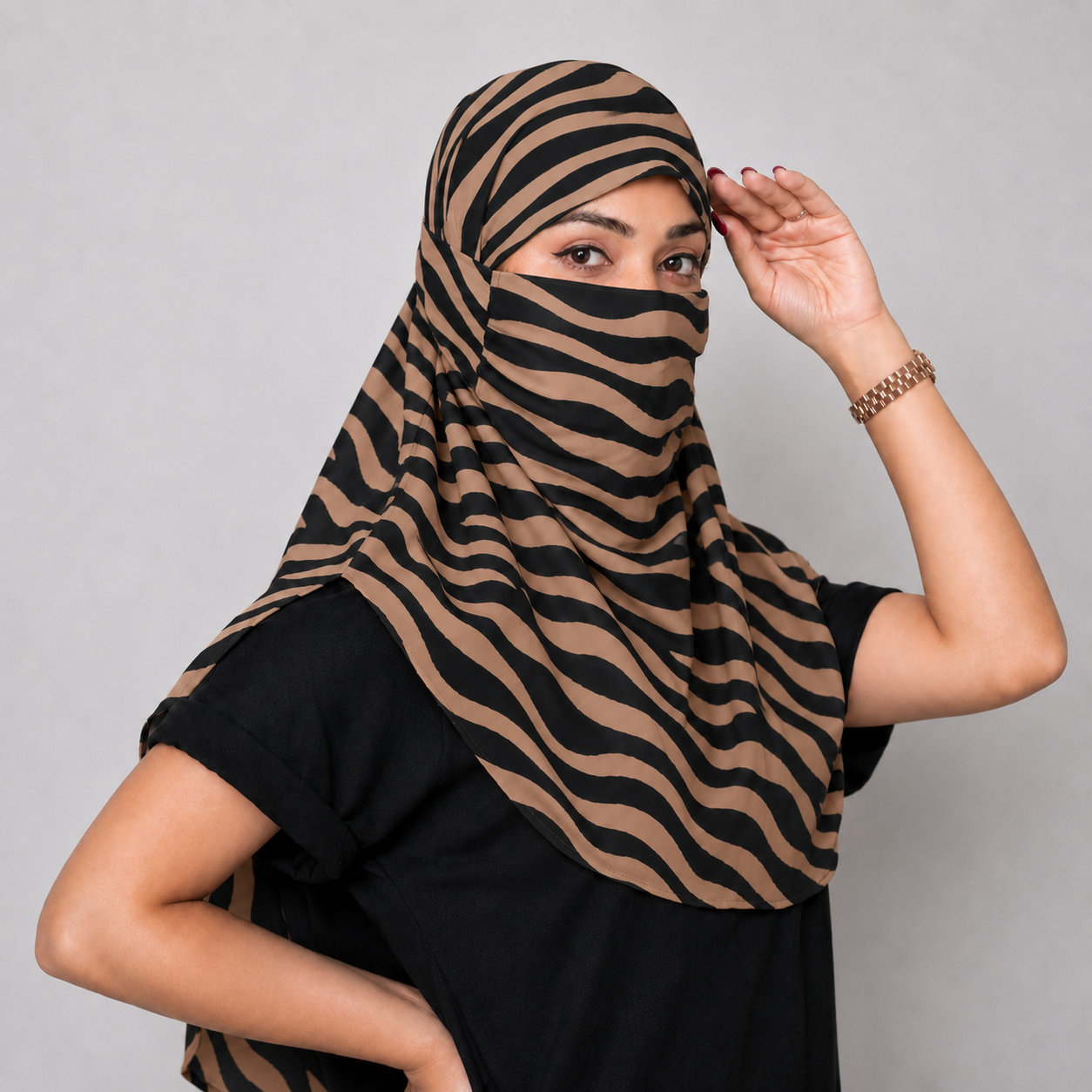 A woman wearing a black and tan zebra-print face scarf , posing against a solid gray studio background.